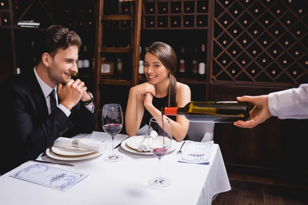 Enfoque selectivo de pareja joven sentada cerca de sommelier vertiendo vino en copa en el restaurante - foto de stock