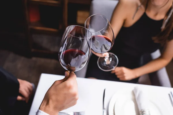 Cropped view of young couple clinking with classes of wine in restaurant — Stock Photo
