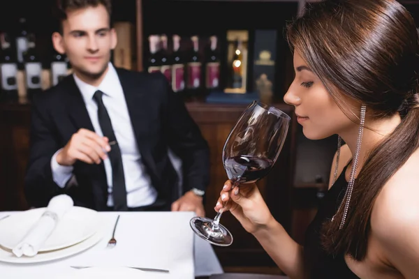 Selective focus of young woman holding glass of wine near boyfriend in restaurant — Stock Photo