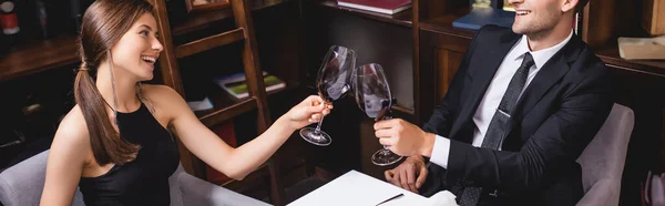 Orientación panorámica de pareja elegante tintineando con vino en restaurante - foto de stock