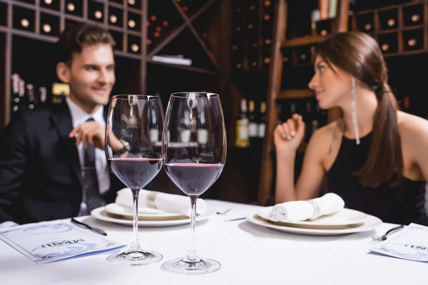 Selective focus of glasses of wine and menu on table near elegant couple in restaurant — Stock Photo