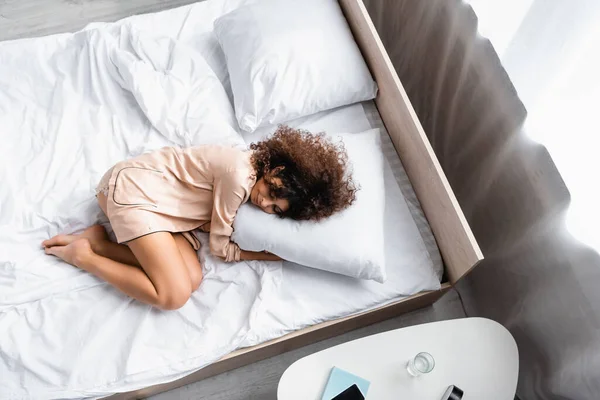 Top view of barefoot woman with closed eyes hugging pillow while sleeping on bed — Stock Photo