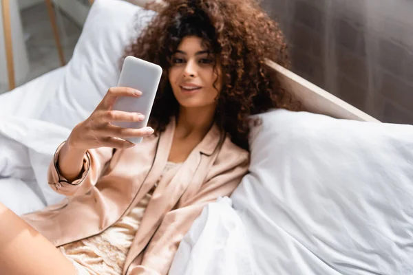 Selektiver Fokus der lockigen Frau, die Selfie im Schlafzimmer macht — Stockfoto
