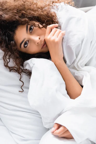 Curly woman wrapped in white blanket looking at camera — Stock Photo