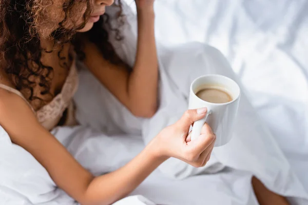 Vista parcial de la mujer rizada sosteniendo la taza de café en la mañana - foto de stock