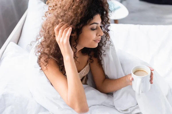 Donna riccia che tocca i capelli e guarda la tazza di caffè al mattino — Foto stock