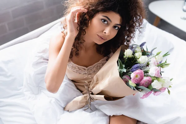 High angle view of curly woman with flowers looking at camera — Stock Photo