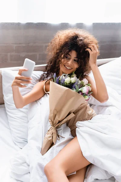 Freudige Frau macht Selfie mit Blumen im Schlafzimmer — Stockfoto