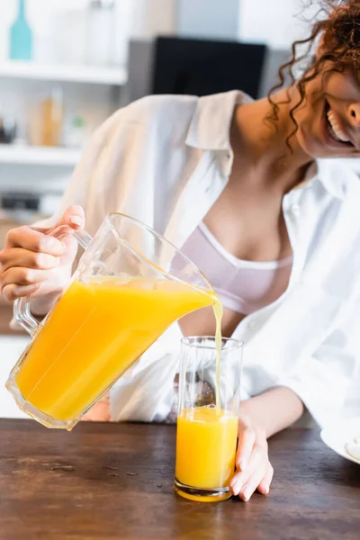 Vista cortada de mulher alegre segurando jarro e derramando suco de laranja fresco — Fotografia de Stock