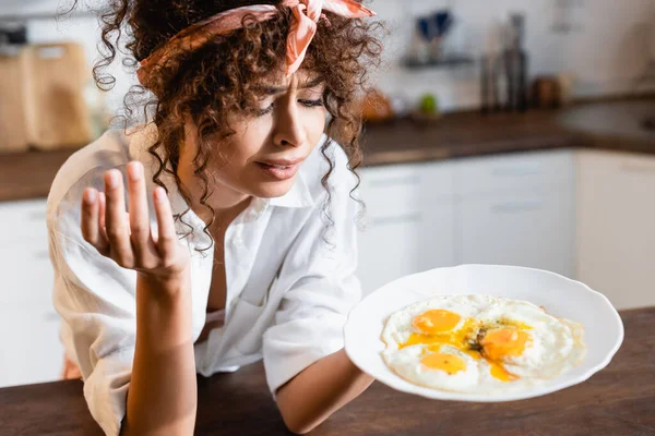 Verwirrte Frau blickt in Küche auf Teller mit Spiegeleiern — Stockfoto