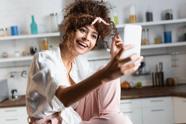 Selective focus of excited woman taking selfie on smartphone in kitchen — Stock Photo