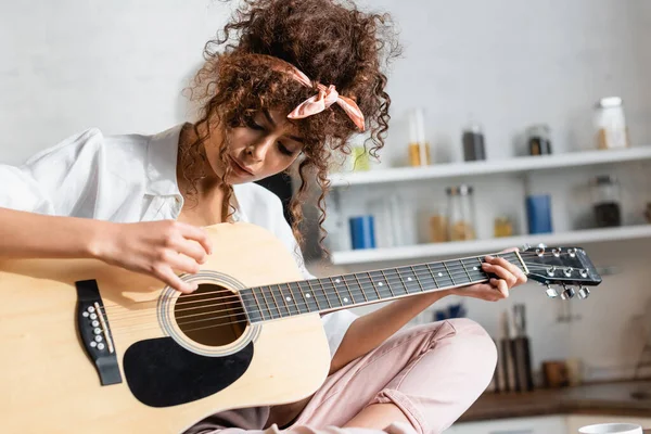 Giovane donna riccia che suona la chitarra acustica a casa — Foto stock