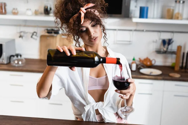 Молода кучерява жінка тримає пляшку і поливає червоне вино в склянці — стокове фото