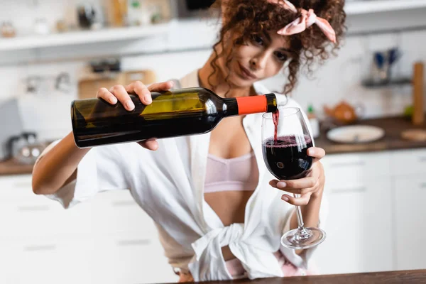 Foco seletivo da mulher encaracolada segurando garrafa e derramando vinho tinto em vidro — Fotografia de Stock