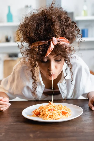 Молодая кудрявая женщина ест вкусные спагетти на кухне — стоковое фото