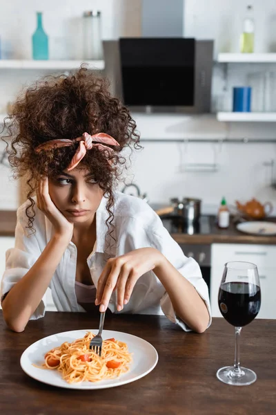 Traurige Frau hält Gabel neben Teller mit vorbereiteten Spaghetti und Glas Wein auf Tisch — Stockfoto