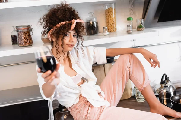 Selective focus of curly woman holding glass of red wine — Stock Photo