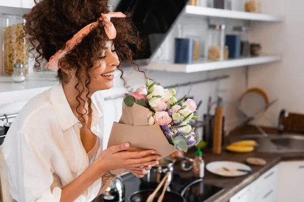 Jeune femme bouclée regardant des fleurs dans la cuisine — Photo de stock