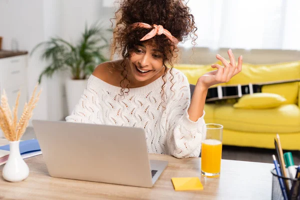Donna gioiosa utilizzando laptop vicino vaso con rami soffici e vetro di succo d'arancia — Foto stock