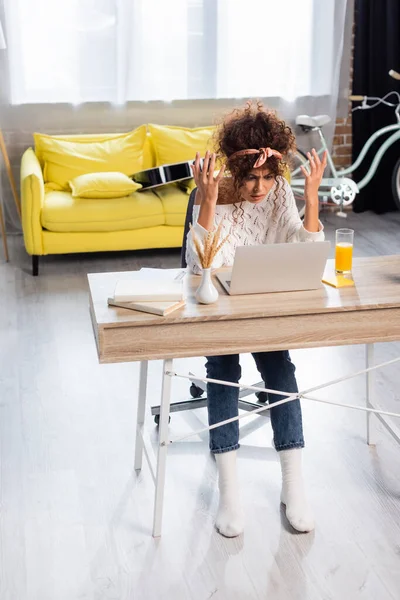 Unzufriedene Freiberufler gestikulieren beim Blick auf Laptop neben Büchern und Glas Orangensaft auf dem Tisch — Stockfoto