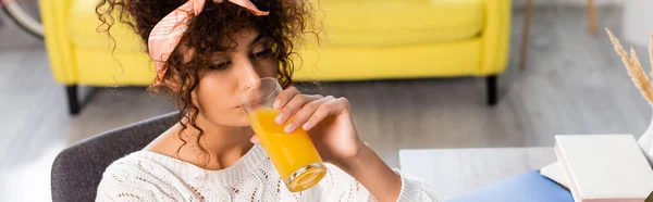 Horizontales Bild einer lockigen Frau, die frischen Orangensaft trinkt — Stockfoto