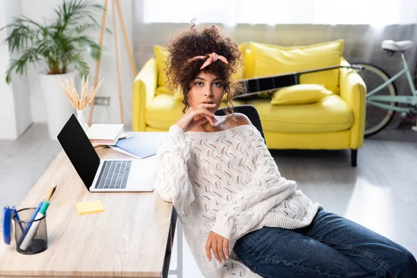 Curly woman sitting near laptop with blank screen on desk — Stock Photo