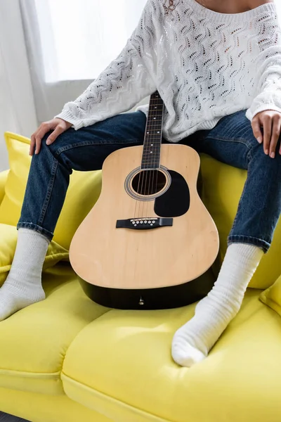 Обрезанный вид женщины, сидящей на диване с акустической гитарой — стоковое фото