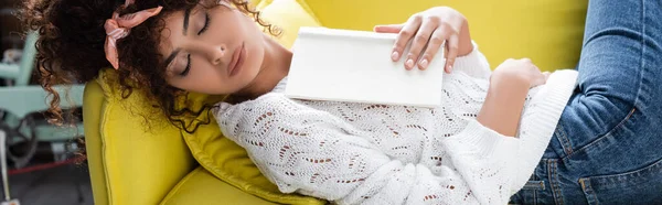 Immagine orizzontale di giovane donna riccia che dorme con libro in soggiorno — Foto stock