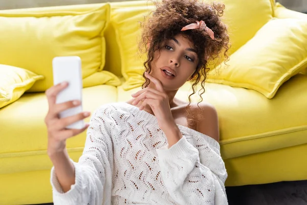 Selective focus of curly woman taking selfie in living room — Stock Photo
