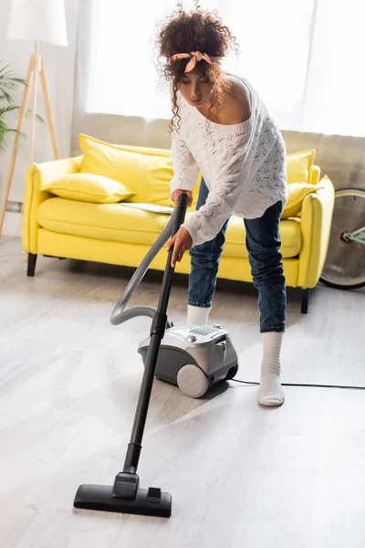 Curly woman in socks using vacuum cleaner while cleaning home — Stock Photo