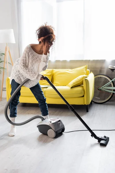 Jeune femme en chaussettes en utilisant l'aspirateur tout en nettoyant la maison — Photo de stock