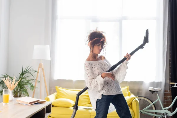 Кудрявая женщина с утиным лицом весело проводит время, держа пылесос и уборка дома — стоковое фото