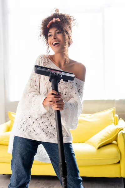 Mujer emocionada divirtiéndose mientras sostiene la aspiradora y la limpieza en casa — Stock Photo