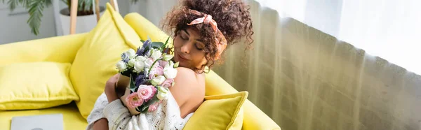 Imagem horizontal da jovem com olhos fechados segurando buquê e flores cheirosas na sala de estar — Fotografia de Stock