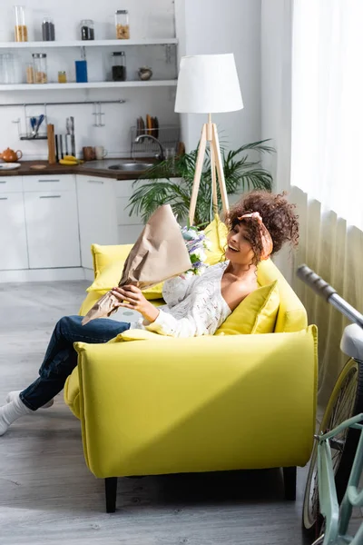 Excited young woman looking at bouquet of flowers and gesturing in living room — Stock Photo