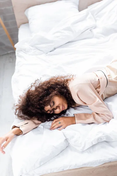 Visão de alto ângulo de encaracolado e jovem mulher com olhos fechados dormindo na cama — Fotografia de Stock