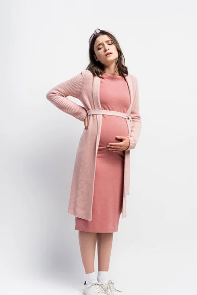 Upset and pregnant woman in headband touching belly while having cramp on white — Stock Photo