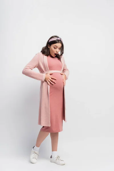 Vue pleine longueur de la femme choquée et enceinte regardant le ventre sur blanc — Photo de stock