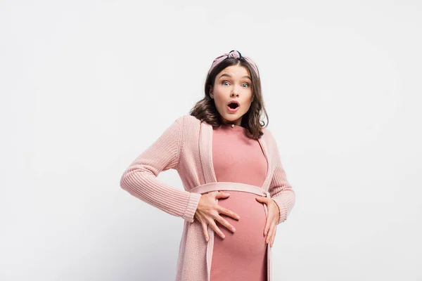 Mulher chocada e grávida olhando para a câmera e tocando barriga no branco — Fotografia de Stock