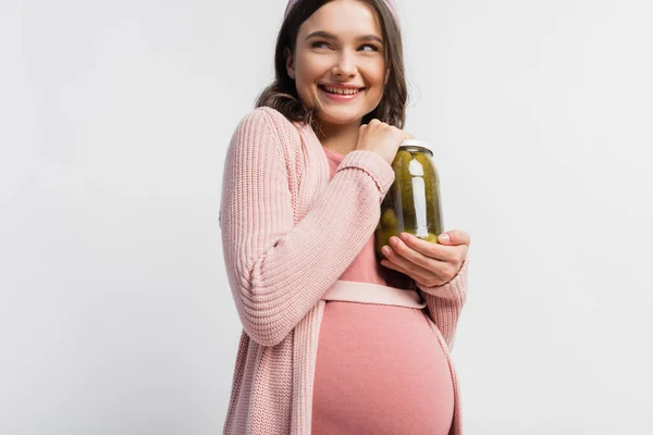 Mujer alegre y embarazada sosteniendo frasco con pepinos en escabeche aislados en blanco - foto de stock