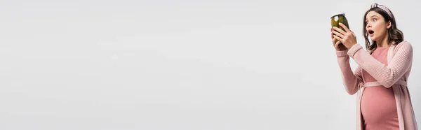 Панорамний урожай шокованої і вагітної жінки, що тримає банку з маринованими огірками, ізольовані на білому — стокове фото