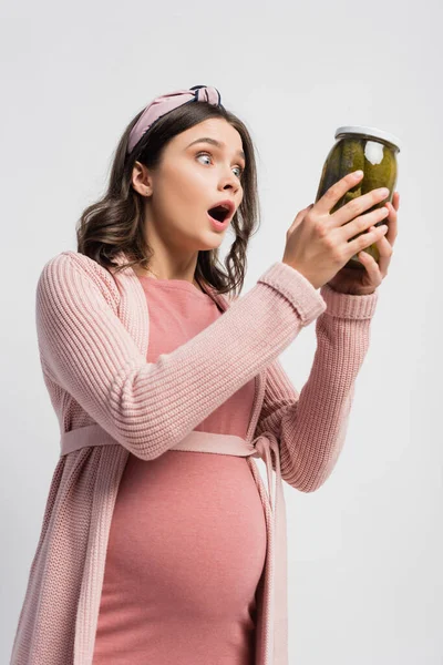 Shocked and pregnant woman holding jar with pickled cucumbers isolated on white — Stock Photo