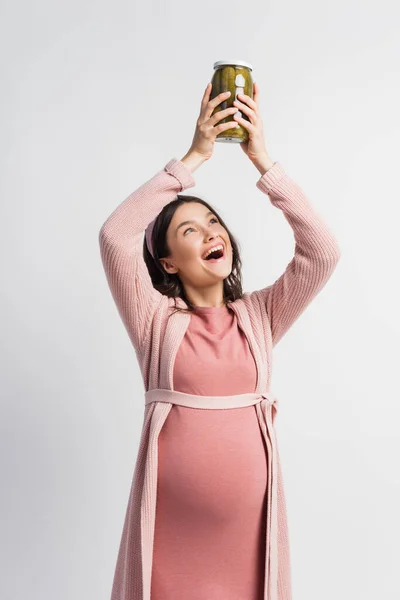 Excited and pregnant woman holding jar with pickled cucumbers above head isolated on white — Stock Photo