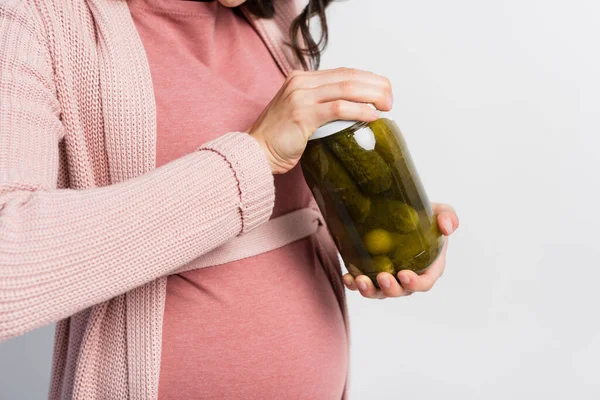 Vista recortada de mujer embarazada abriendo tarro con pepinos agrios y encurtidos aislados en blanco - foto de stock