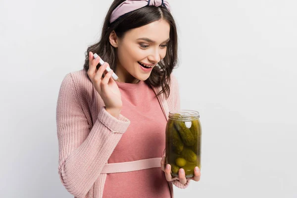 Donna eccitata e incinta guardando vaso con cetrioli acidulo e sottaceto isolato su bianco — Foto stock