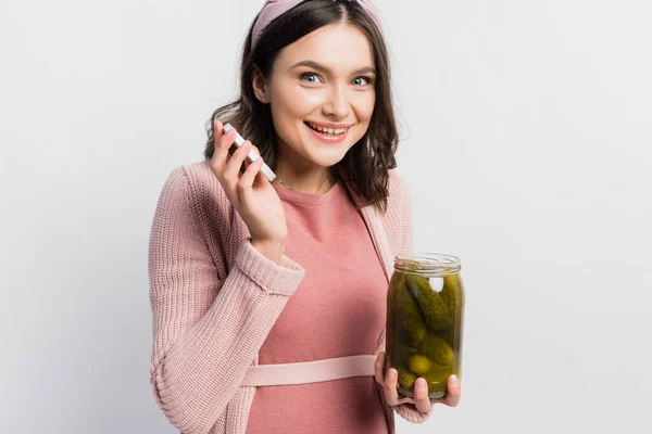 Joyful and pregnant woman holding jar with pickled cucumbers isolated on white — Stock Photo