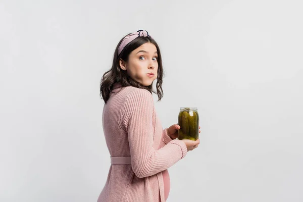 Surprised and pregnant woman holding jar while eating pickled cucumbers isolated on white — Stock Photo