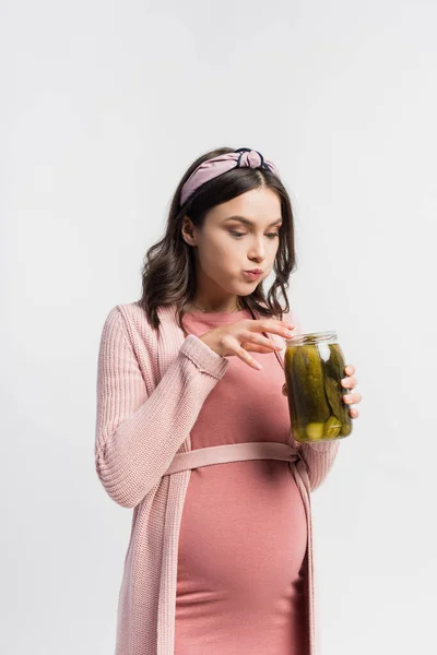 Hungry pregnant woman looking at jar with pickled cucumbers isolated on white — Stock Photo