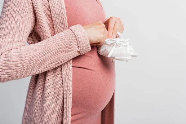 Vista parcial de la mujer embarazada sosteniendo botas de bebé aisladas en blanco - foto de stock