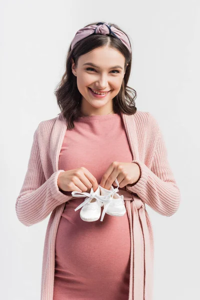Freudige und schwangere Frau mit winzigen Babystiefeln auf weißem Grund — Stockfoto